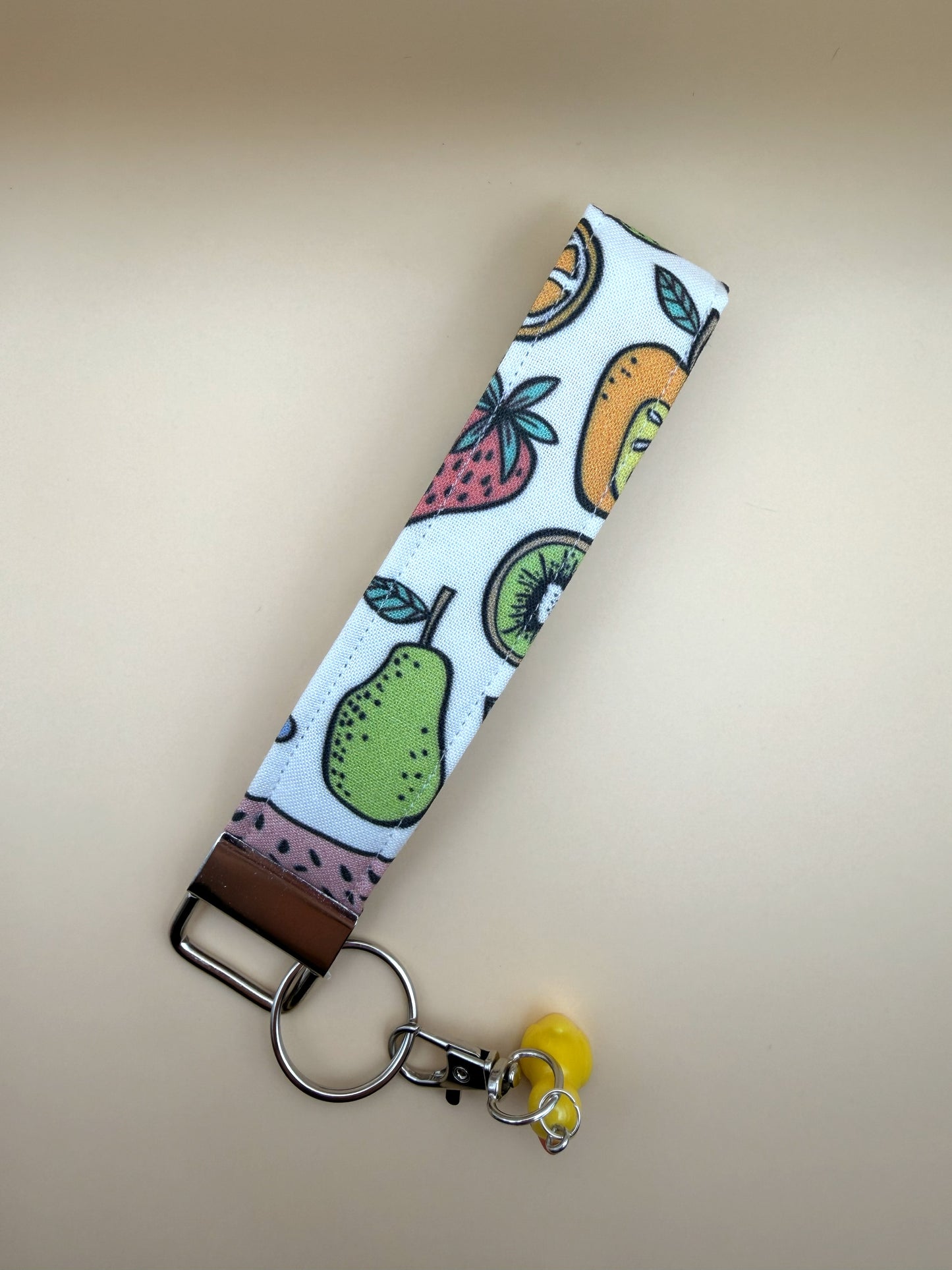 Fruit-patterned keychain strap with a yellow charm on a beige background